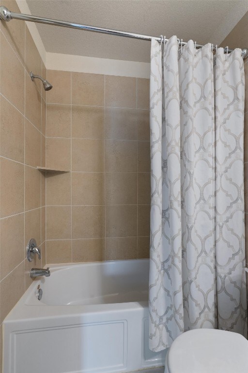 bathroom with toilet, shower / tub combo with curtain, and a textured ceiling