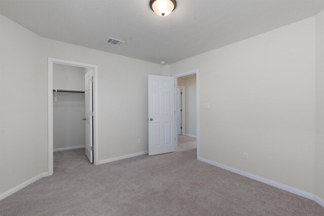 unfurnished bedroom with a closet, light colored carpet, and a walk in closet