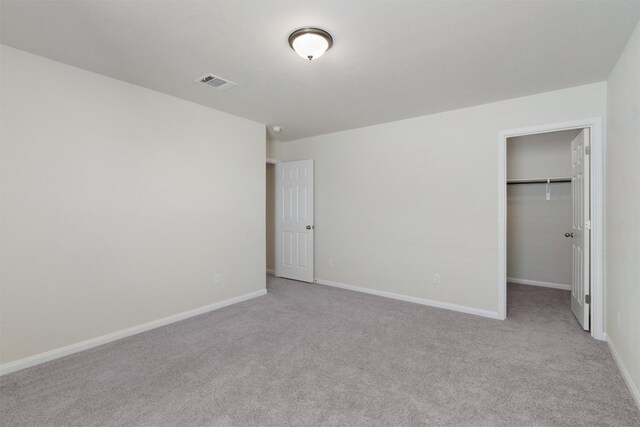 unfurnished bedroom featuring a closet, a walk in closet, and light colored carpet