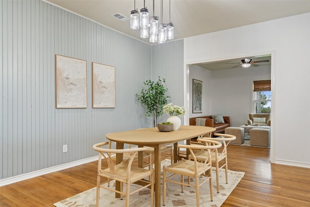 dining area featuring ceiling fan with notable chandelier, wooden walls, and light hardwood / wood-style flooring