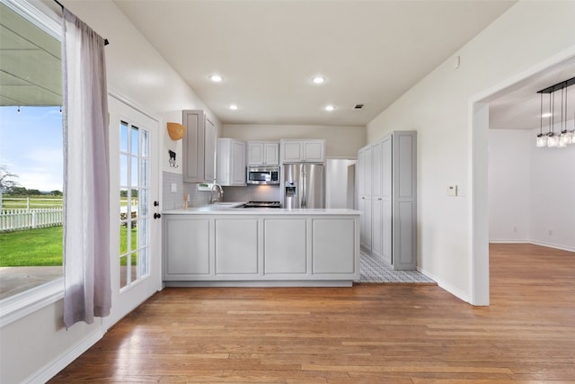 kitchen with light hardwood / wood-style flooring, decorative light fixtures, stainless steel appliances, sink, and tasteful backsplash