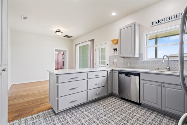 kitchen with a wealth of natural light, stainless steel dishwasher, kitchen peninsula, and gray cabinets