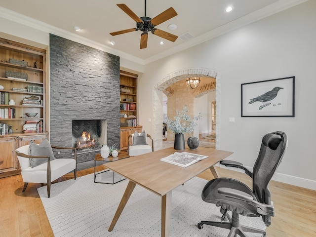 office with built in shelves, a stone fireplace, ornamental molding, and light hardwood / wood-style floors