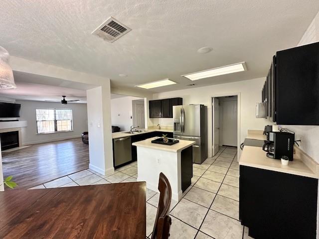 kitchen with a textured ceiling, ceiling fan, light tile floors, and stainless steel appliances