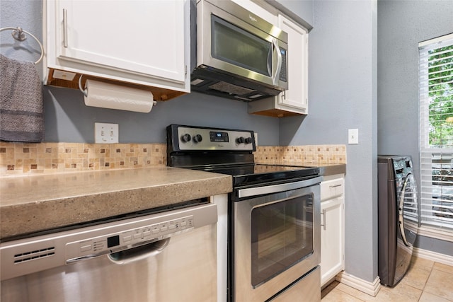 kitchen with appliances with stainless steel finishes, tasteful backsplash, light tile floors, washer / dryer, and white cabinetry