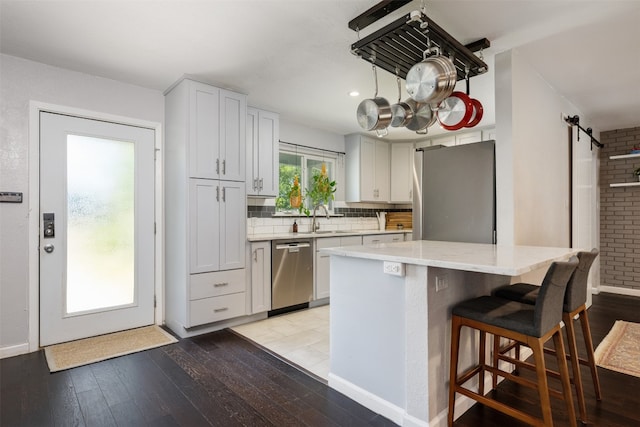 kitchen featuring sink, light hardwood / wood-style flooring, stainless steel appliances, light stone countertops, and a barn door