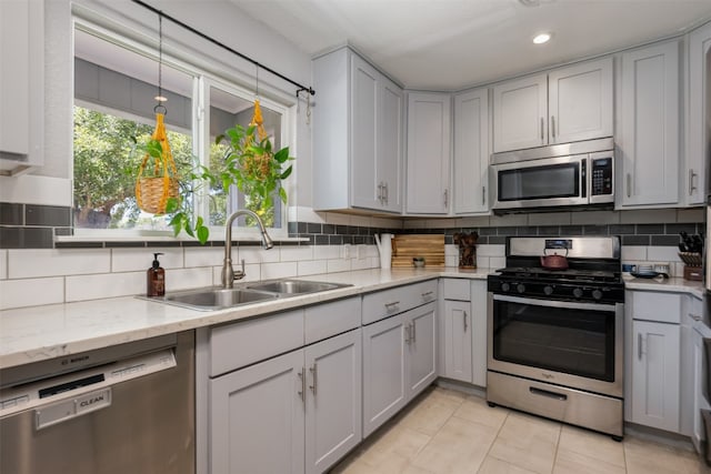 kitchen featuring appliances with stainless steel finishes, sink, backsplash, and light stone counters