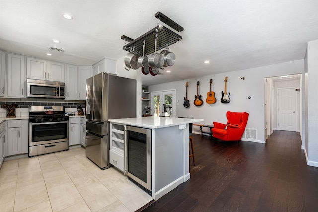 kitchen with backsplash, appliances with stainless steel finishes, beverage cooler, gray cabinets, and a breakfast bar area