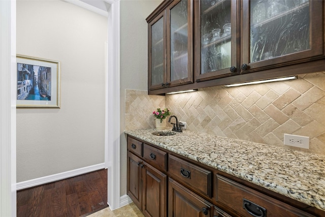 bar featuring backsplash, light stone counters, dark brown cabinetry, and light hardwood / wood-style flooring