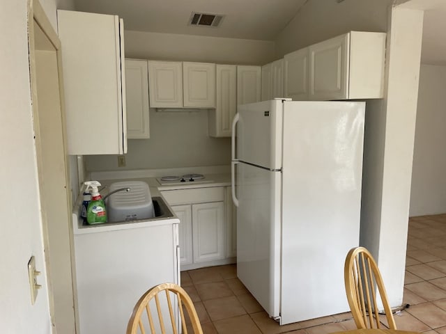 kitchen with light tile floors, white cabinets, lofted ceiling, and white refrigerator