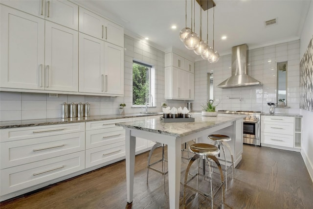 kitchen featuring white cabinets, high end range, dark wood-style flooring, wall chimney range hood, and a kitchen bar