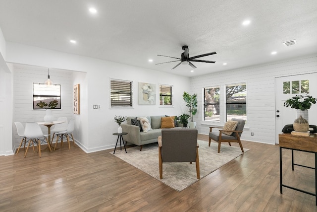 living room with wood walls, a textured ceiling, wood-type flooring, and ceiling fan