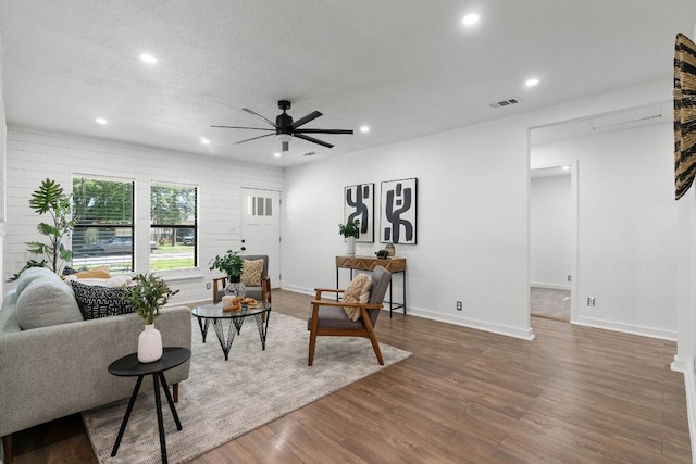 living room featuring dark hardwood / wood-style flooring, ceiling fan, and a textured ceiling