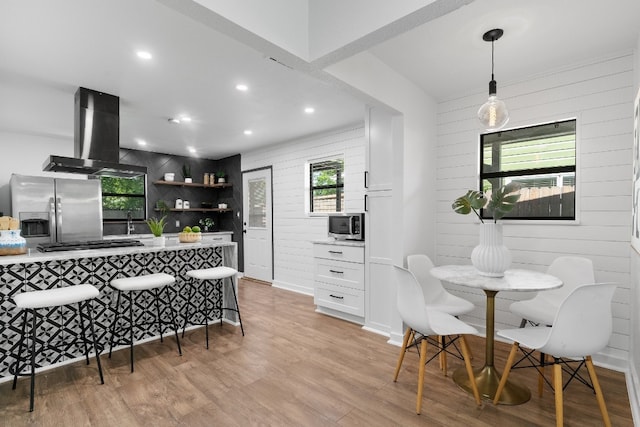 kitchen featuring decorative light fixtures, white cabinetry, appliances with stainless steel finishes, light hardwood / wood-style flooring, and wall chimney exhaust hood