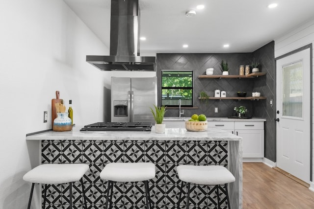 bar with stainless steel fridge, light hardwood / wood-style floors, white cabinets, backsplash, and range hood