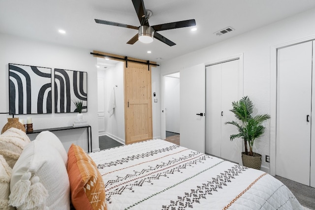 bedroom featuring a barn door, ceiling fan, and dark hardwood / wood-style floors