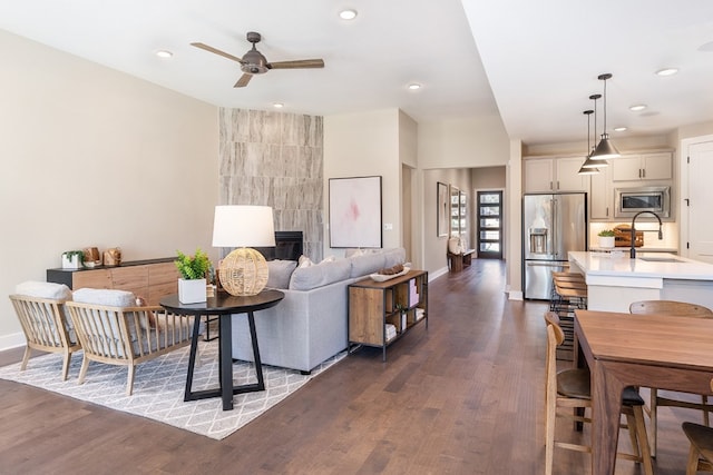 living room featuring ceiling fan, a large fireplace, sink, and dark wood-type flooring