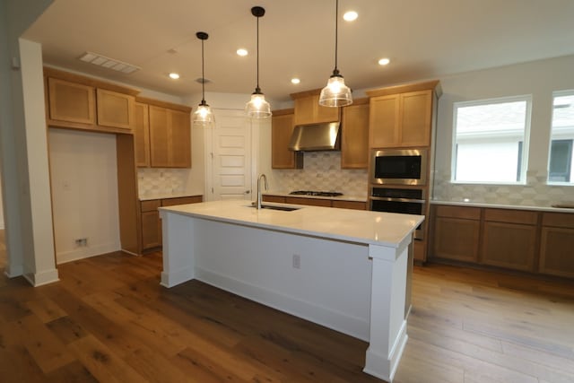 kitchen featuring hanging light fixtures, stainless steel appliances, dark hardwood / wood-style floors, range hood, and a kitchen island with sink