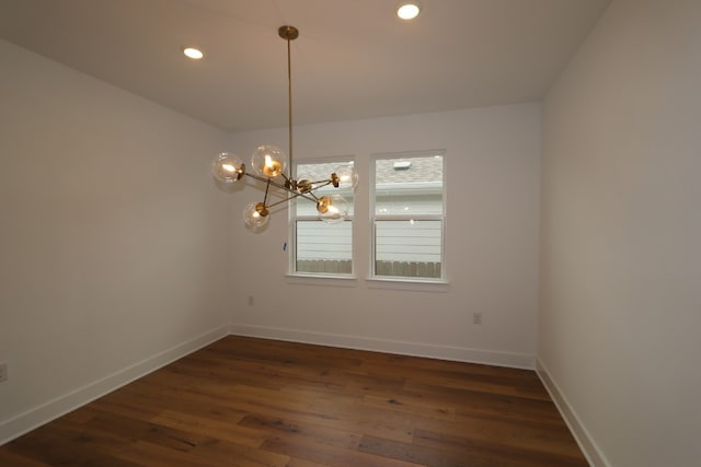 spare room featuring dark wood-type flooring and a notable chandelier