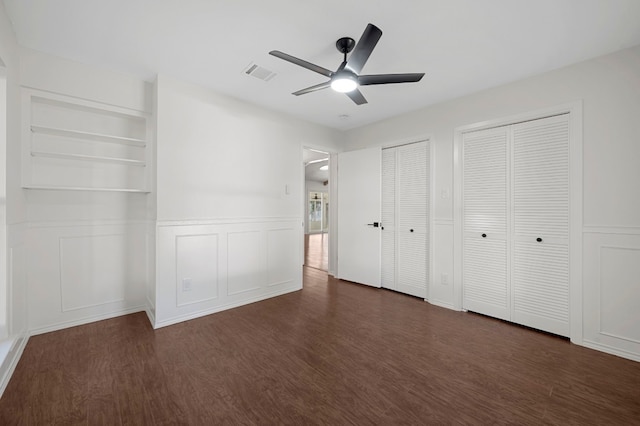 unfurnished bedroom with two closets, dark hardwood / wood-style floors, and ceiling fan