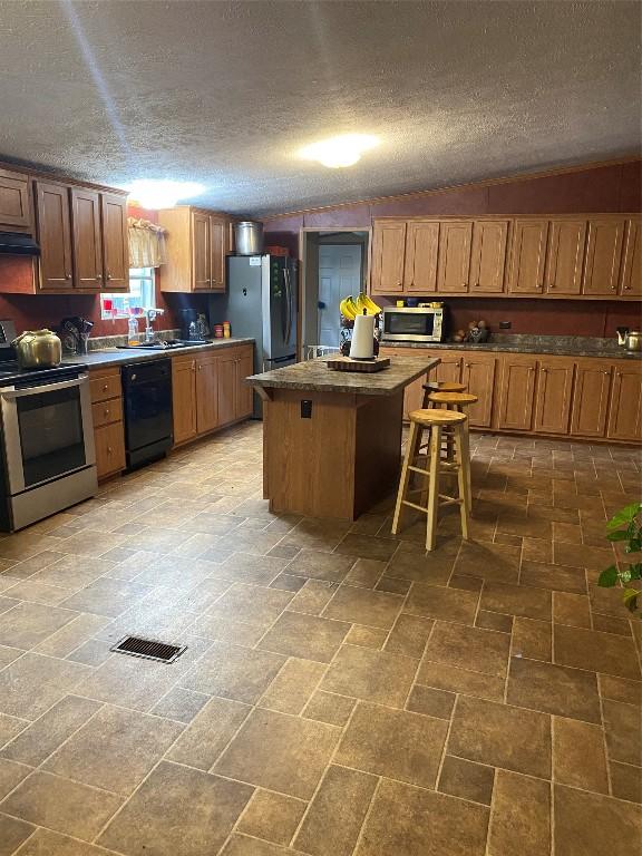 kitchen with stainless steel appliances, a center island, brown cabinets, and a kitchen bar