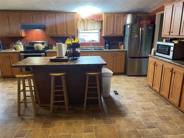 kitchen featuring a center island, stainless steel appliances, dark countertops, a sink, and a kitchen bar