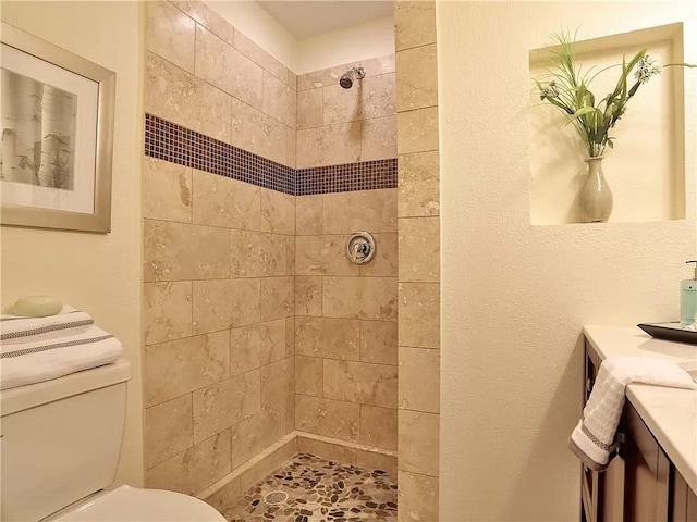 bathroom featuring tiled shower, toilet, and vanity