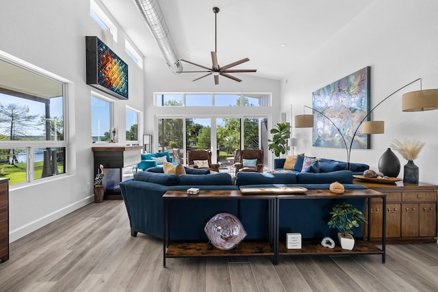 living room with a high ceiling, ceiling fan, plenty of natural light, and light hardwood / wood-style flooring