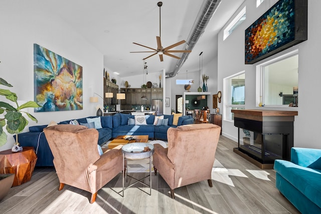 living room with a multi sided fireplace, light hardwood / wood-style flooring, high vaulted ceiling, and ceiling fan