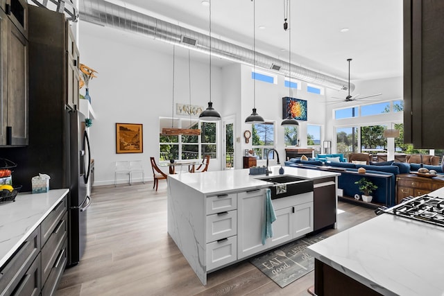 kitchen with white cabinetry, a high ceiling, hanging light fixtures, and a kitchen island with sink