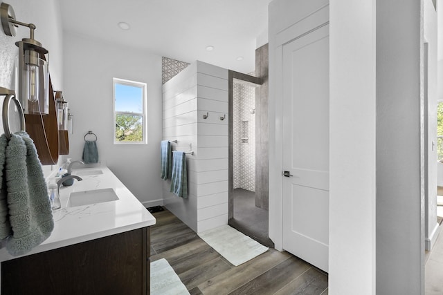 bathroom with hardwood / wood-style flooring, tiled shower, and vanity