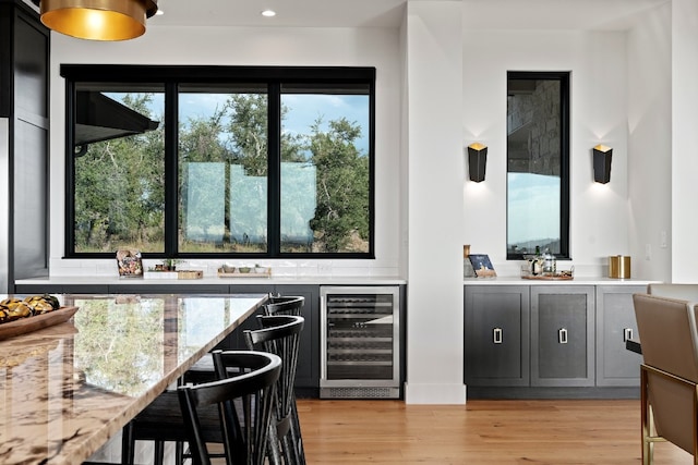 kitchen with light stone counters, light wood-type flooring, and beverage cooler