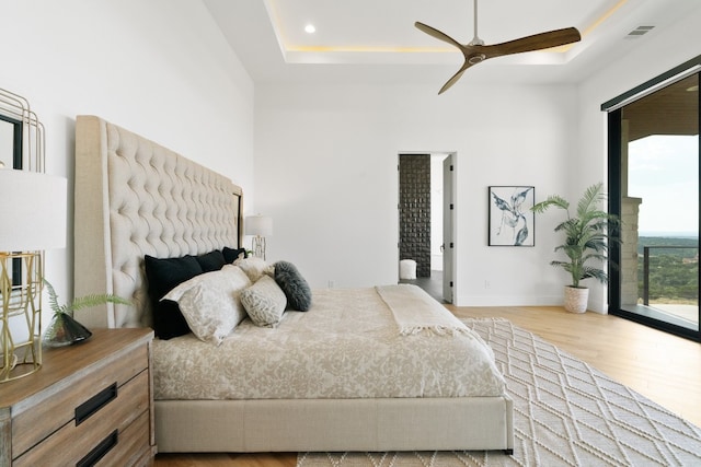 bedroom featuring hardwood / wood-style floors, ceiling fan, a raised ceiling, and access to outside