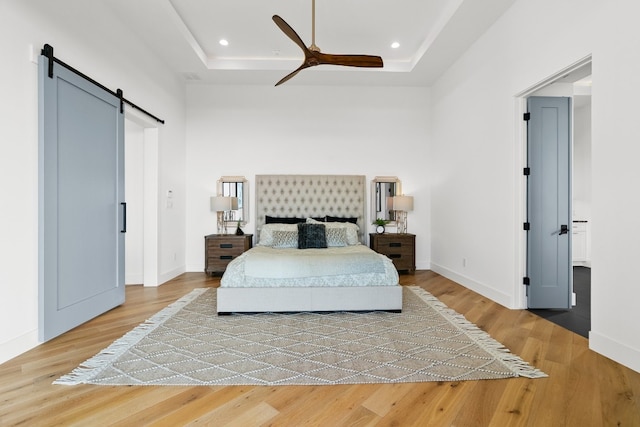 bedroom with light hardwood / wood-style flooring, ceiling fan, a tray ceiling, and a barn door