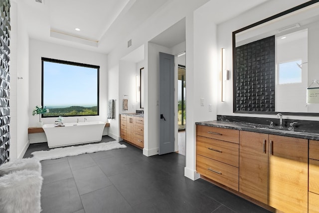 bathroom with a washtub, a tray ceiling, vanity with extensive cabinet space, and tile flooring