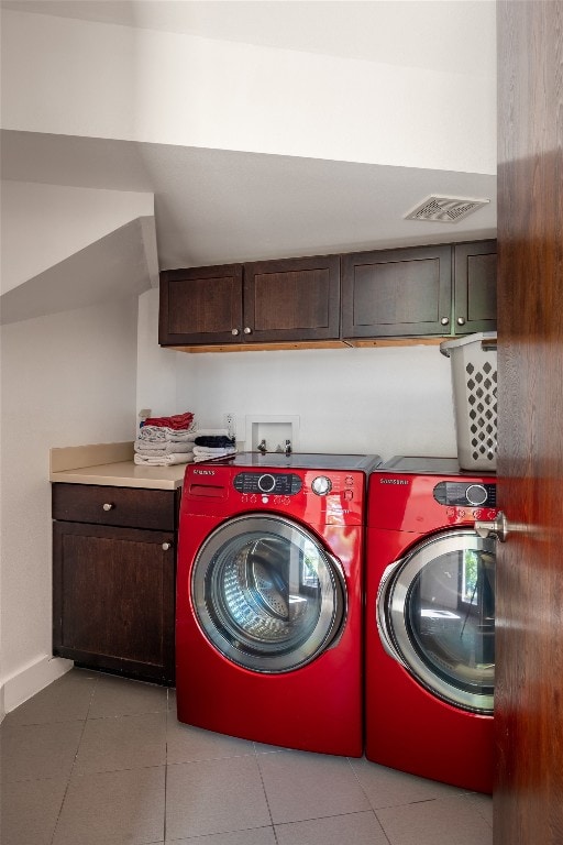 clothes washing area featuring cabinets, light tile patterned floors, and washing machine and clothes dryer