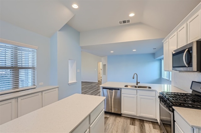 kitchen with appliances with stainless steel finishes, white cabinets, light wood-type flooring, lofted ceiling, and sink