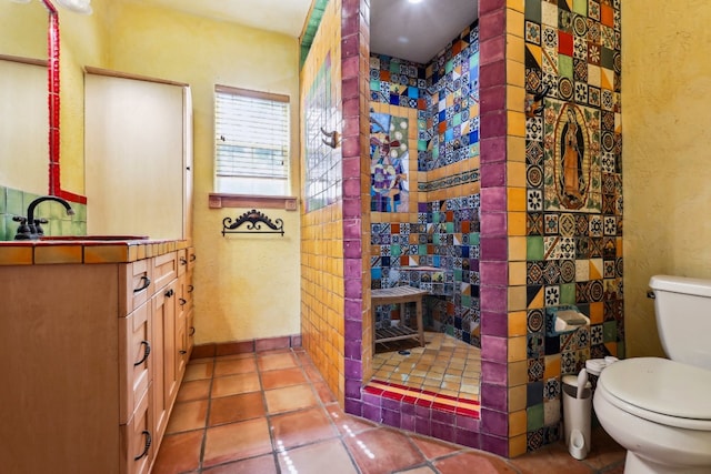 bathroom with tile flooring, toilet, a tile shower, and vanity