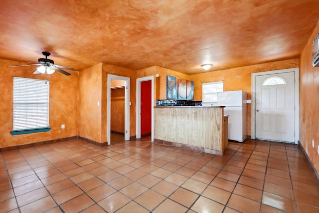 kitchen featuring ceiling fan, white fridge, tile floors, and kitchen peninsula