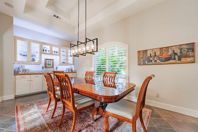 tiled dining room featuring an inviting chandelier and a raised ceiling