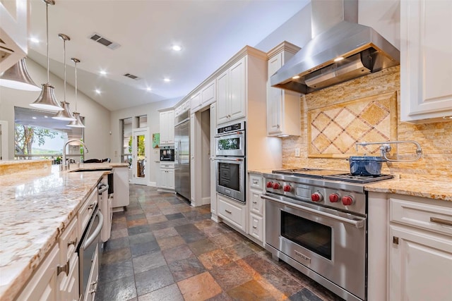 kitchen featuring pendant lighting, white cabinets, high end appliances, decorative backsplash, and wall chimney exhaust hood