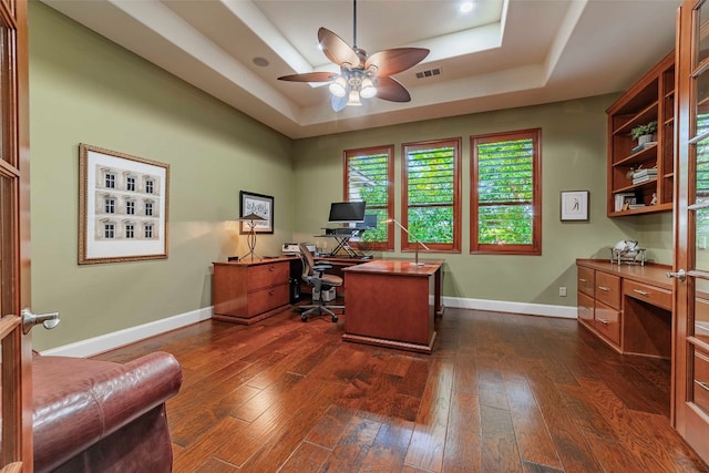 home office featuring dark wood-type flooring, ceiling fan, and a raised ceiling