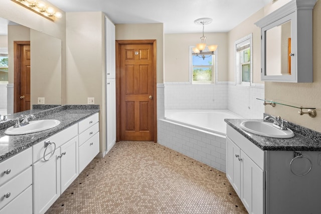 bathroom with tiled bath, tile flooring, dual vanity, and an inviting chandelier