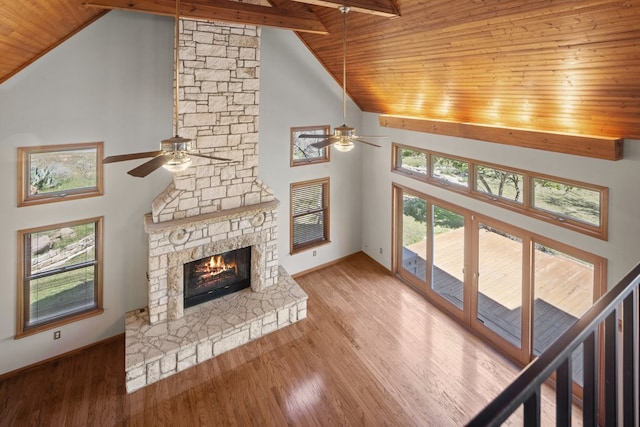 unfurnished living room featuring ceiling fan, light hardwood / wood-style floors, a fireplace, high vaulted ceiling, and beam ceiling