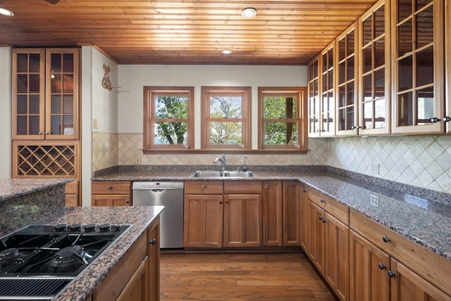 kitchen with stainless steel dishwasher, dark stone countertops, hardwood / wood-style floors, backsplash, and sink