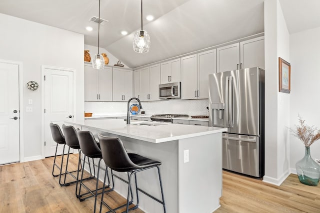 kitchen featuring pendant lighting, light wood-type flooring, stainless steel appliances, vaulted ceiling, and a kitchen island with sink