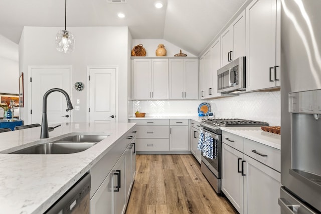 kitchen featuring appliances with stainless steel finishes, backsplash, light hardwood / wood-style floors, decorative light fixtures, and sink