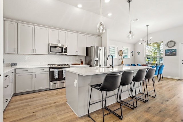 kitchen featuring appliances with stainless steel finishes, a chandelier, light wood-type flooring, a center island with sink, and hanging light fixtures