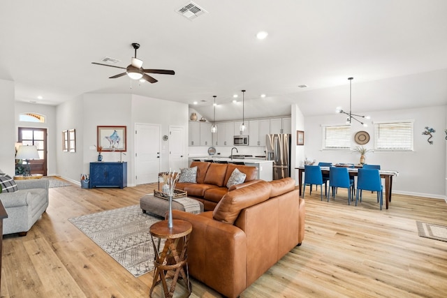 living room with ceiling fan with notable chandelier, light hardwood / wood-style floors, and plenty of natural light