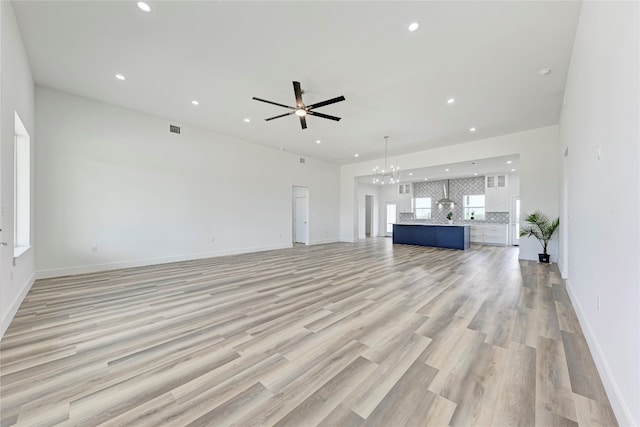 unfurnished living room with plenty of natural light, ceiling fan with notable chandelier, and light wood-type flooring